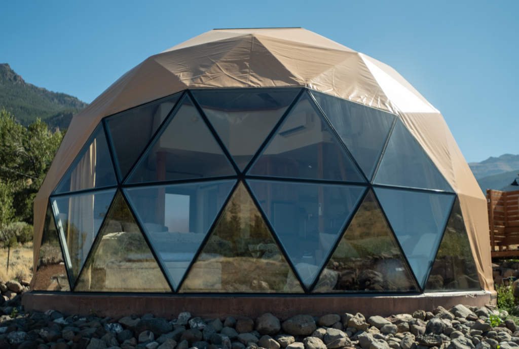 Front view of Heart Mountain lodging dome, glass windows facing mountains and mountains in the background, blue sky